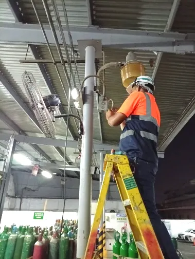 Técnico sobre escalera dando mantenimiento a luminarias en planta industrial de gases